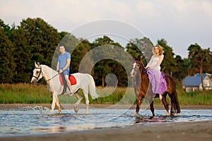 Two riders on horseback at sunset on the beach. Lovers ride horseback. Young beautiful man and woman with a horse at the sea. Rom