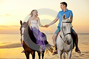 Two riders on horseback at sunset on the beach. Lovers ride horseback. Young beautiful man and woman with a horses at the sea.