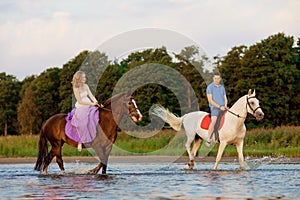 Two riders on horseback at sunset on the beach. Lovers ride horseback. Young beautiful man and woman with a horses at the sea.