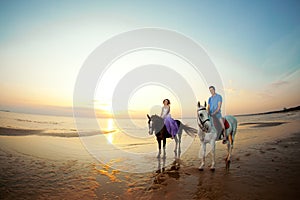 Two riders on horseback at sunset on the beach. Lovers ride horseback. Young beautiful man and woman with a horses at the sea.