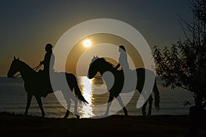 Two riders riding during sunset on the seashore