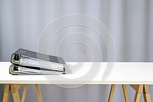 Two ring binders lying on a simple white desk on wooden racks, grey background with copy space, office or business concept