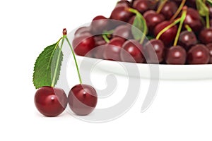 Two ripe berries with green leaf and plate of cherry (isolated)