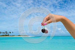 Two ripe cherries on women hand at tropical beach