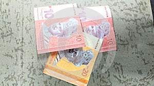 Two RM10 and one RM20 Malaysian Ringgit banknotes placed on a textured surface.