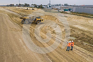 Two road construction workers in orange vests and protective helmets in the middle on the field