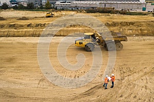 Two road construction workers in orange vests and protective helmets in the middle on the field