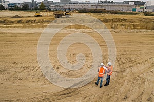 Two road construction workers in orange vests and protective helmets in the middle on the field