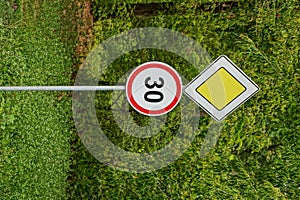 Two road signs near the road against the background of green branches and grass