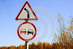 Two road signs warning no overtaking and turning right against a blue sky