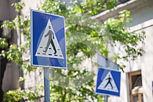 Two roadsigns warning drivers of the presence of a crosswalk with pedestrians crossing in an urban landscape