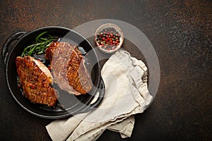 Two roasted duck breast fillets with crispy skin, with pepper and rosemary, top view in black cast iron pan with knife