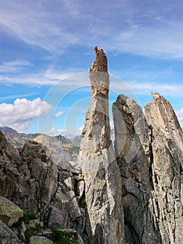 Two rock climbers sitting atop a sharp rock needle in the Val Bregaglia