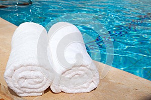 Two rolled-up white towels by blue pool