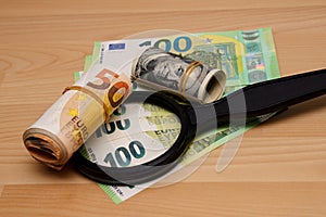 Two rolls of dollars and euros on one hundred euro banknotes next to a magnifying glass