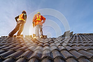 Two Roofer workers in protective uniform wear and gloves, using air or pneumatic nail gun and installing Concrete Roof Tiles on