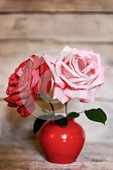 Two roses in red vase on aged wooden background