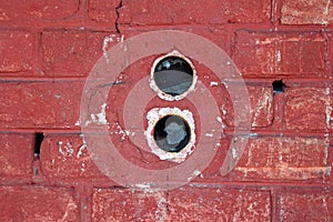 Two round electrical outlet boxes without wires mounted inside dilapidated red brick wall