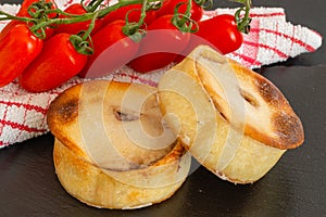 Two Round Scotch Pies on Black Slate Serving Tray with Red Checked Teatowel and Cherry Red Vine Tomatoes