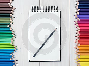 Two rows of colored pencils and notebook on wooden background