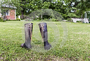 Two rubber boots on a green lawn near red house in farm