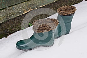 Two rubber winter green boots with brown fur on white snow