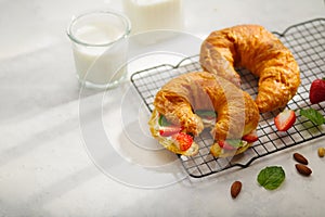 Two ruddy croissants with fresh strawberries, mint leaves, almonds and milk on a white plate. Restaurant, hotel, cafe, pastry shop