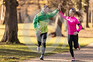 Two runners mature man and young woman support each other and give high-five while a run
