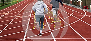 Two runners running over six iinch hurdles in lane on a track