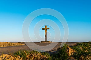 Two rural roads intersect at a big old Christian stone cross in front of a clear blue sky at the beginning sunset