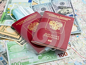 Two Russian passports are on dollar and euro bills. A medical mask is attached to one of the passports. The concept of traveling
