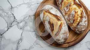 Two rustic bread loaves on wooden platter marble counter