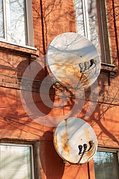 Two rusty satellite dishes on the wall of a red brick building