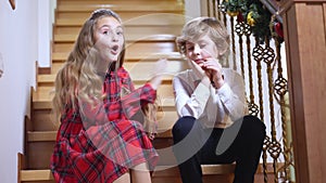 Two sad children sitting on stairs on Christmas eve with dog noticing something pointing away rubbing hands smiling