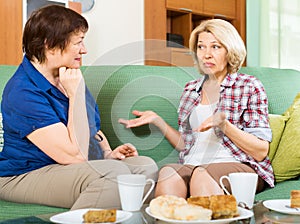 Two sad elderly women chating on couch