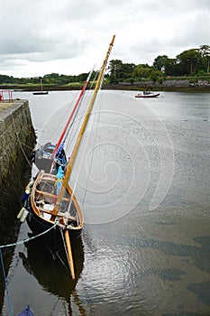 Two wooden sailboats anchored against a stone seawall in a protected harbor in rural Ireland