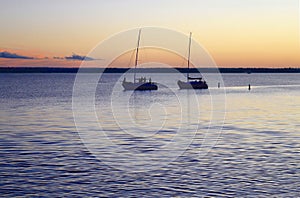 Two sailboats returning to their dock at sunset