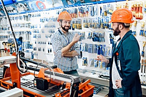 Two salesmen are discussing equipment selection near woodworking machine in power tools store.