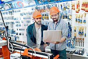 Two salesmen are discussing equipment selection near woodworking machine in power tools store.