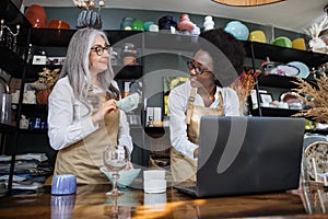 Two saleswomen counting goods at shop using laptop photo