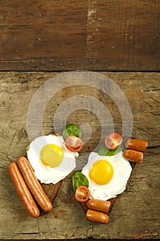 Two sandwiches Fried eggs with sausages and tomatoes with herbs on a piece of bread on a wooden table.