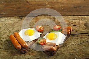 Two sandwiches Fried eggs with sausages and tomatoes with herbs on a piece of bread on a wooden table.