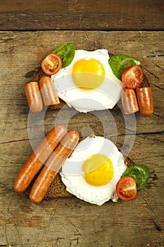 Two sandwiches Fried eggs with sausages and tomatoes with herbs on a piece of bread on a wooden table.