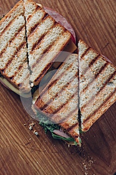 Two sandwiches on a wooden background, top view. Stack of panini with ham, cheese and lettuce sandwich on a cutting board