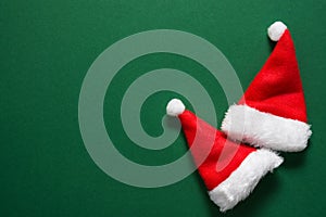 Two Santa Claus hats on solid dark green background. Christmas New Year holiday greeting card poster banner placeholder