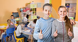 Two satisfied children standing in schoolroom on background with pupils studying