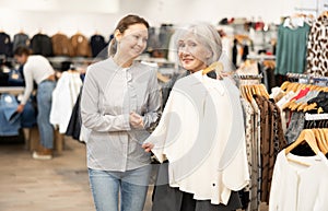 Two satisfied female customers choosing cardigan or jacket in clothing boutique