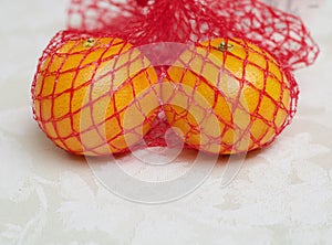 Two satsumas in red nylon net bag standing on damask tablecloth