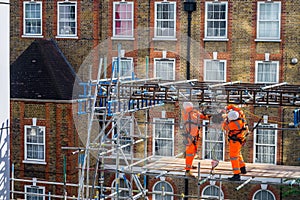 Two scaffolders working on a building site, wearing orange hi-vis protection clothes.