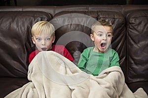 Two scared little boys sitting on a couch watching TV